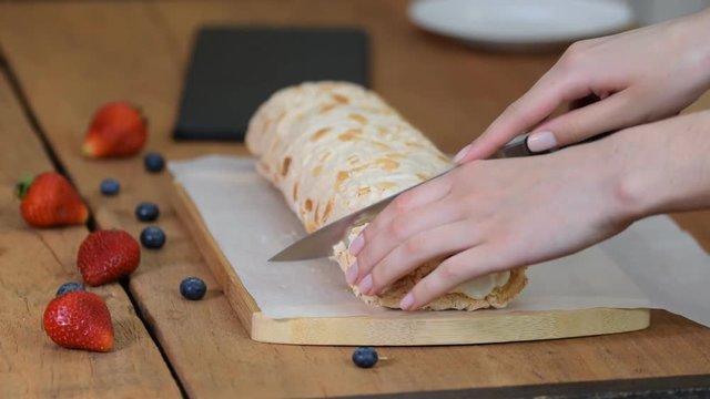Close up, young girl is cutting meringue roulade with berries and mascarpone.