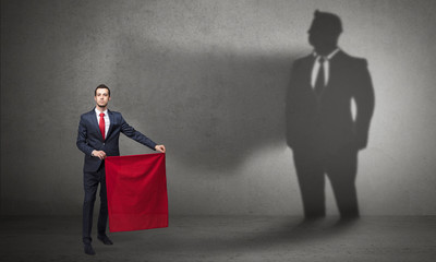 Businessman standing with red cloth on his hand and his shadow on the background
