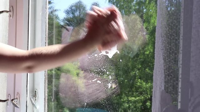 pregnant girl wipes a cloth with foam window on the background of a good summer day, the concept of cleaning the house.