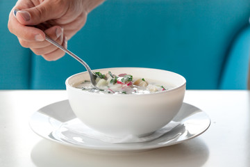 He eats soup okroshka from round white plate