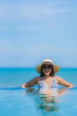 Fototapeta na wymiar Portrait beautiful young asian woman happy smile relax in swimming pool at hotel resort neary sea ocean beach on blue sky