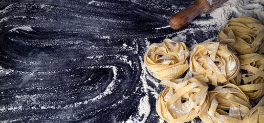 Homemade uncooked pasta on black background. Making fresh italian fettuccine.