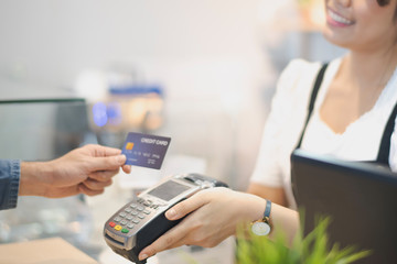 In the Cafe, Customer using credit card Makes a Pays to Woman by cashless technology System. Contact less payment concept.