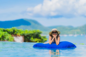 Portrait beautiful young asian woman happy smile relax in swimming pool at hotel resort neary sea ocean beach on blue sky