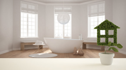 Fototapeta na wymiar White table top or shelf with green plant in pot shaped like house, modern blurred bathroom with bathtub in the background, interior design, real estate, eco architecture concept idea