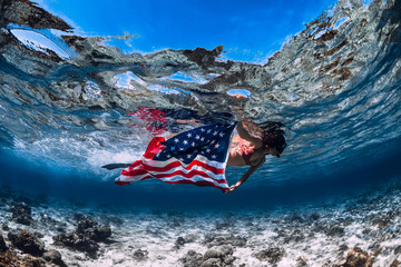Beautiful girl freediver swim over sandy sea bottom with United States flag. Independence day.