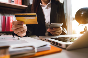 businesswoman hand using smart phone, tablet payments and holding credit card online shopping, omni channel, digital tablet docking keyboard computer at office in sun light