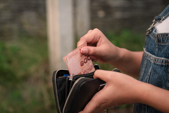 Casual young Asian girl taking 100 Baht banknote out of her purse to pay - Ethnic Thai woman holding Thailand paper currency money cash to pay for street food outdoors in the day