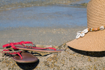 sandals and hat on the rocks of the beach with the sea in the background