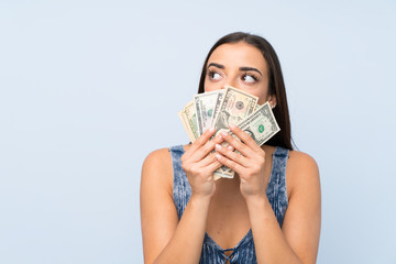 Young woman over isolated blue wall taking a lot of money