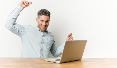 Young handsome man working with his laptop celebrating a special day, jumps and raise arms with energy.