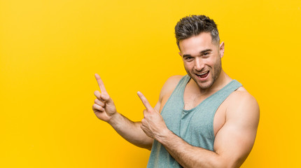 Young fitness man against a yellow background pointing with forefingers to a copy space, expressing excitement and desire.