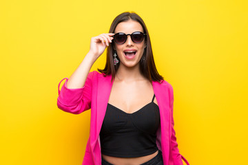 Young woman over isolated yellow background with glasses and surprised