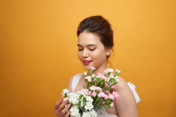 Portrait of a pretty young woman holding bouquet of carnation isolated over yellow background