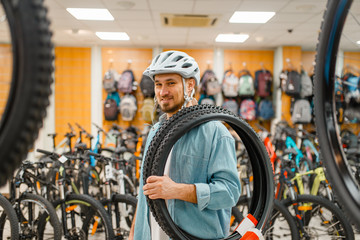 Fototapeta na wymiar Man in cycling helmet holds bicycle tyre, shopping