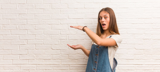 Young hipster woman holding something very surprised and shocked