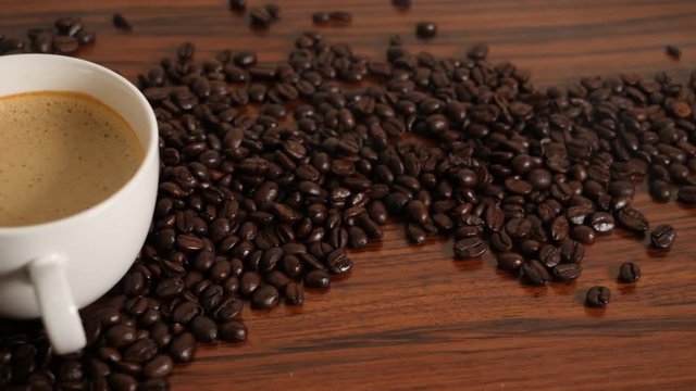 Slowmotion Pan shot of coffee cup surrounded by coffee beans.