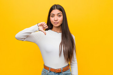 Young pretty arab woman against a yellow background showing a dislike gesture, thumbs down....