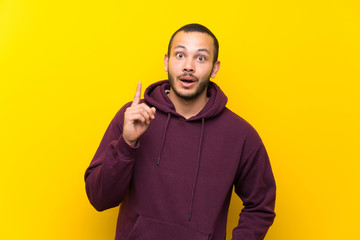 Colombian man with sweatshirt over yellow wall thinking an idea pointing the finger up