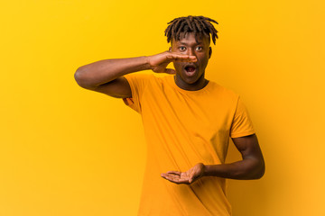 Young black man wearing rastas over yellow background holding something with both hands, product...