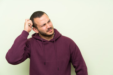 Colombian man with sweatshirt over green wall having doubts and with confuse face expression