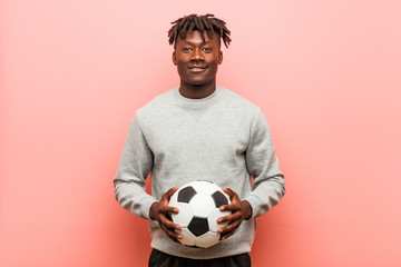 Young fitness black man holding a soccer ball happy, smiling and cheerful.