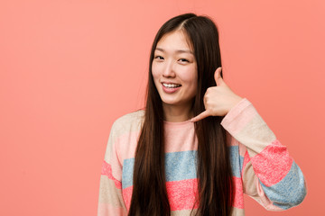 Young cool chinese woman showing a mobile phone call gesture with fingers.