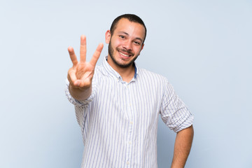 Fototapeta premium Colombian man over isolated blue wall happy and counting three with fingers