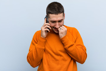 Young caucasian man holding a phone biting fingernails, nervous and very anxious.