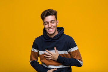 Young cool man wearing a hoodie laughs happily and has fun keeping hands on stomach.