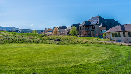 Obraz premium Panorama frame Residential houses on a terrain with vivid green grasses viewed on a sunny day