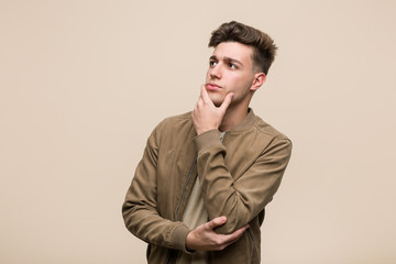 Young caucasian man wearing a brown jacket looking sideways with doubtful and skeptical expression.