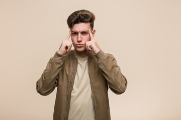 Young caucasian man wearing a brown jacket focused on a task, keeping him forefingers pointing head.