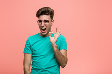 Young cool caucasian man winks an eye and holds an okay gesture with hand.
