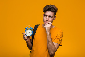 Young student man holding an alarm clock cheering carefree and excited. Victory concept.