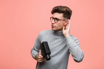 Young intellectual man holding a film camera trying to listening a gossip.