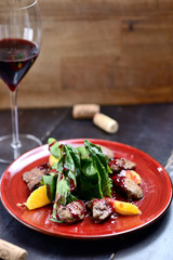 salad with liver, spinach and orange on a red plate, on a wooden table