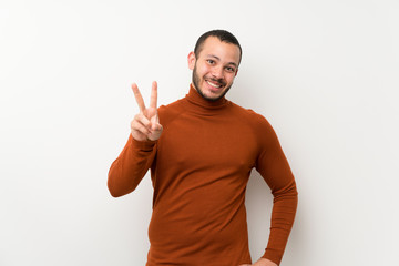 Naklejka premium Colombian man with turtleneck sweater smiling and showing victory sign