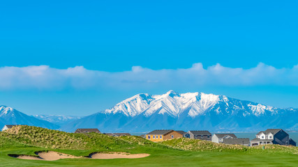 Panorama Lush grassy terrain with a view of lake and snow capped mountain under blue sky