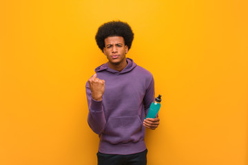 Young african american fitness man holding an energy drink showing fist to front, angry expression