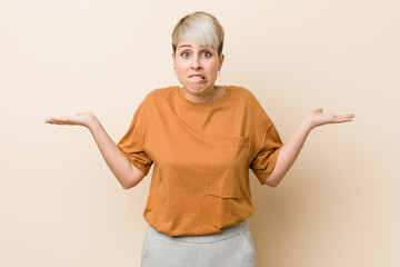 Young plus size woman with short hair confused and doubtful shrugging shoulders to hold a copy space.