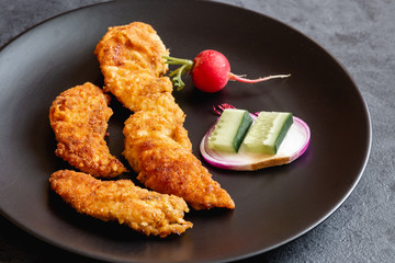 Fried chicken sirloin in breadcrumbs on a black dish.