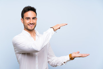 Handsome young man over isolated blue background holding copyspace to insert an ad