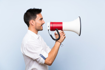 Handsome young man over isolated blue background shouting through a megaphone