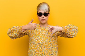 Young curvy woman wearing a floral summer clothes showing thumbs up and thumbs down, difficult...