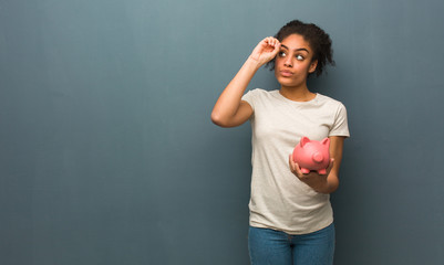 Young black woman making the gesture of a spyglass. She is holding a piggy bank.