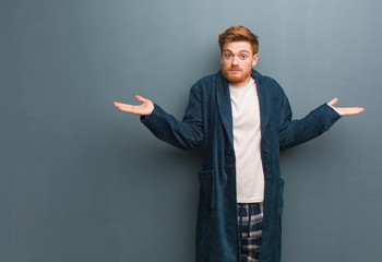 Young redhead man in pajama confused and doubtful