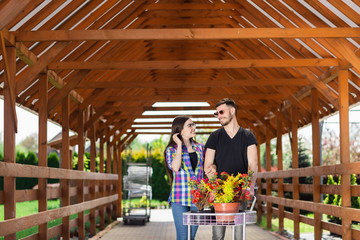 Young couple with a carriage full of different plants in the greenhouse