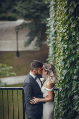 Naklejka premium Beautiful bride in a long white dress. Handsome groom in a black suit. Couple in a summer park