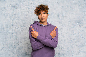 Young african american man over grunge wall pointing to the laterals having doubts